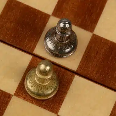 Deux pions doré et argenté face à face sur l'échiquier d'acajou