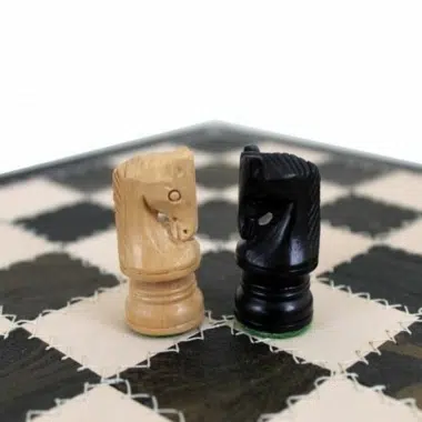 Détail des deux cavaliers en bois clair et noir sur l'échiquier en cuir
