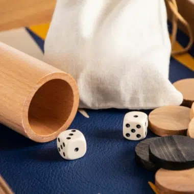 Gros plan sur les dés blancs et les pions bois posés sur le similicuir bleu