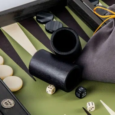 Gobelets à dés noirs, dés et pochette de rangement sur le plateau vert olive